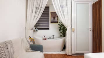 A bathroom with a bathtub, a shower, a sink, and a mirror. There is a plant and a bottle of lotion on the sink counter.