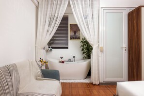 A bathroom with a bathtub, a shower, a sink, and a mirror. There is a plant and a bottle of lotion on the sink counter. - Aura Retreat Hanoi Central (Ha Noi)