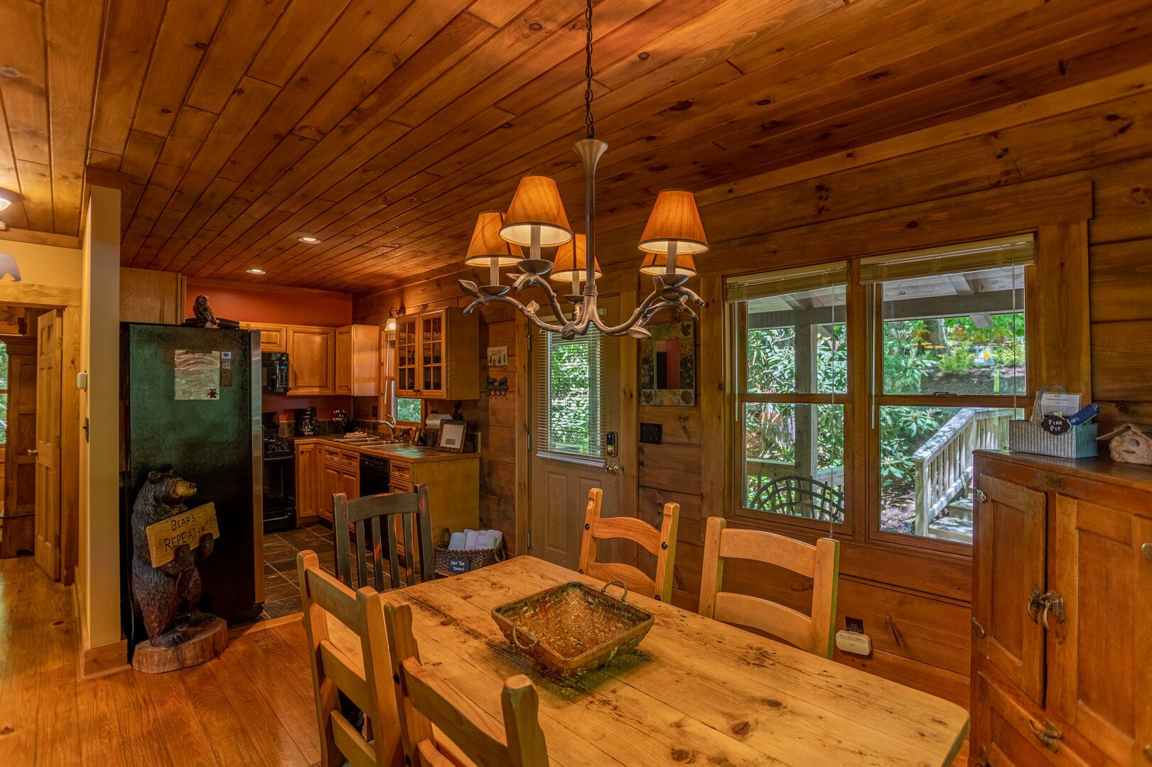 Ein Interieur einer Holzhütte mit einem Esstisch, Stühlen, einer Chandelieber und einem Kühlschrank mit Bär-Dekoration.