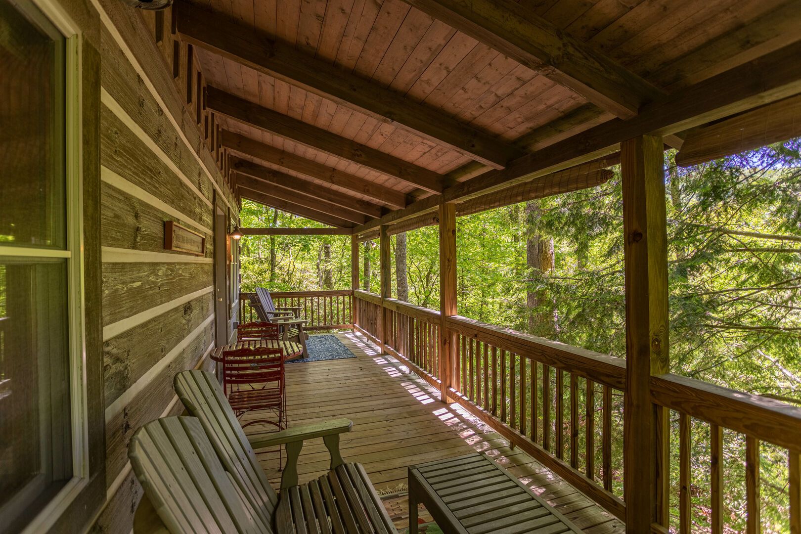 A wooden porch with a view of a forest. There are benches and a table.