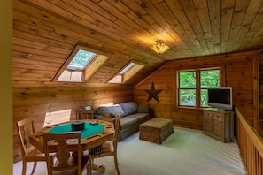 A cozy room with a wooden ceiling, a star decoration, a television, a sofa, a table with a pool table, and a window with a view of trees. - Private Mountain Retreat with Hot Tub, Fire Pit & Forest Views (Vilas)