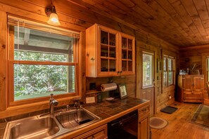 A wooden cabin interior with a kitchen area, including a sink, cabinets, and a dishwasher. - Private Mountain Retreat with Hot Tub, Fire Pit & Forest Views (Vilas)