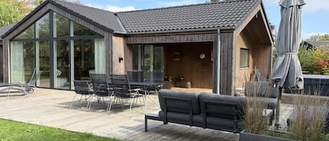 Una casa moderna con terraza, mobiliario exterior y un ventanal amplio.