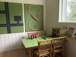 A room with a green table, wicker chairs, a toy train track, and children's books on a shelf. - "Pirka" - 500m from the sea by Interhome (Væggerløse)