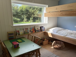 Une chambre d’enfant avec un lit superposé, une table avec des jouets éducatifs et une fenêtre donnant sur un paysage verdoyant.