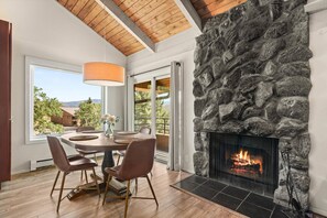 A dining area with a stone fireplace, wooden ceiling, and a view of the outdoors. - Cozy Snowmass Retreat with Vaulted Ceilings, Gas Fireplace, Outdoor HT. On Free Shuttle (Snowmass Village)