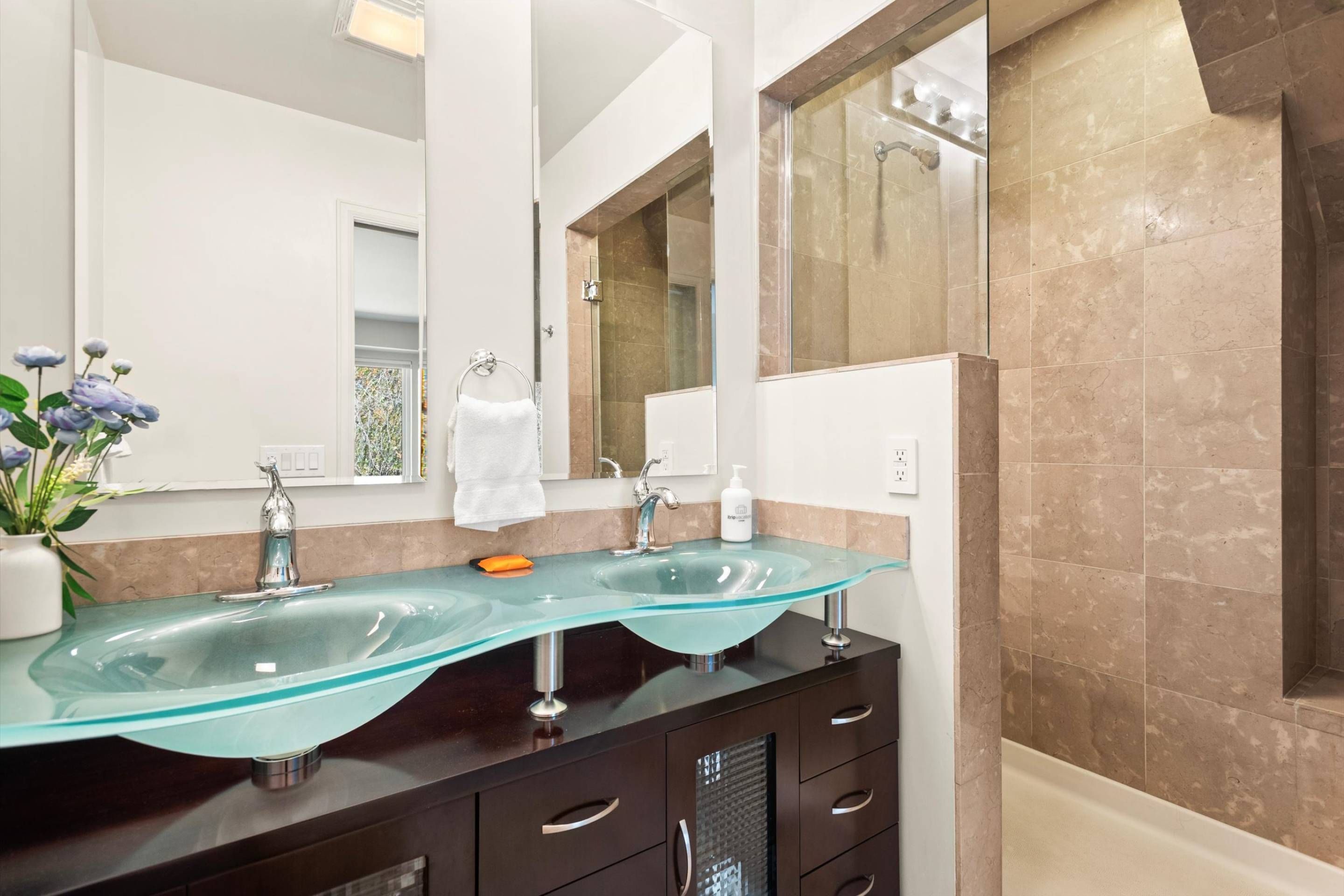 A modern bathroom with a glass sink, dark cabinetry, and a large mirror.