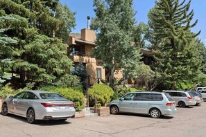 A parking lot with several cars, surrounded by trees and a building with a balcony. - Cozy Snowmass Retreat with Vaulted Ceilings, Gas Fireplace, Outdoor HT. On Free Shuttle (Snowmass Village)