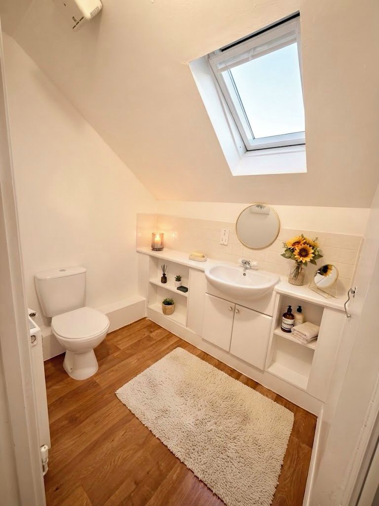 Une petite salle de bain blanche, avec un puits de lumière, des toilettes blanches, un lavabo et un miroir.