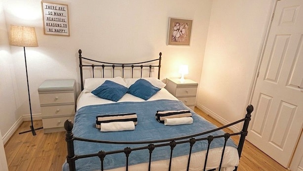 Una cama bien hecha con edredón azul y blanco, una lámpara de noche y un cuadro colgado en la pared.