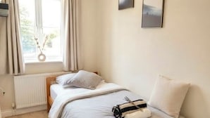 Un dormitorio con una cama, una ventana con cortinas, un radiador y una lámpara colgante.