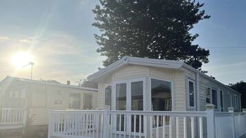 Une maison mobile dotée d’une terrasse clôturée, de grandes fenêtres et offrant une vue sur un ciel dégagé.