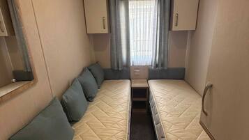 Un intérieur de camping-car compact comprenant deux lits, une petite kitchenette et une fenêtre avec des rideaux.