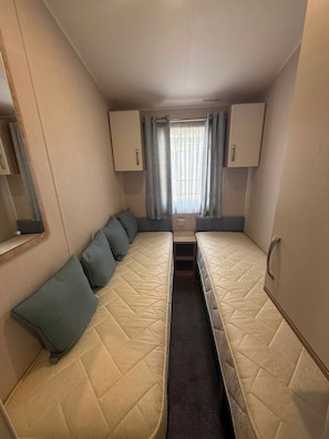 A compact RV interior with two beds, a small kitchenette, and a window with curtains.