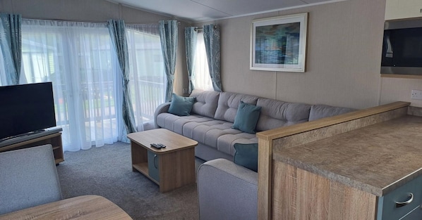 A compact living space with a sofa, a coffee table, a TV, and a kitchenette area.