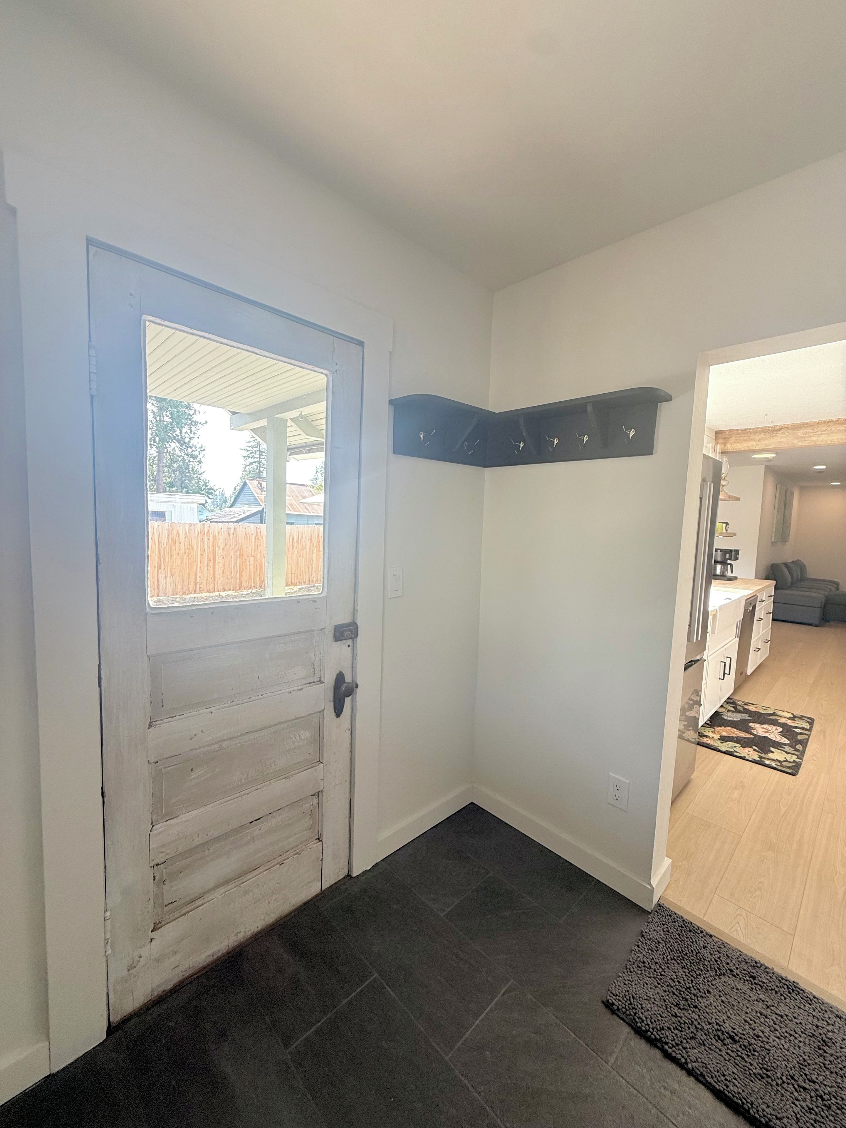 A hallway with a door leading to a room, a dark rug, and a kitchen area visible through an open door.