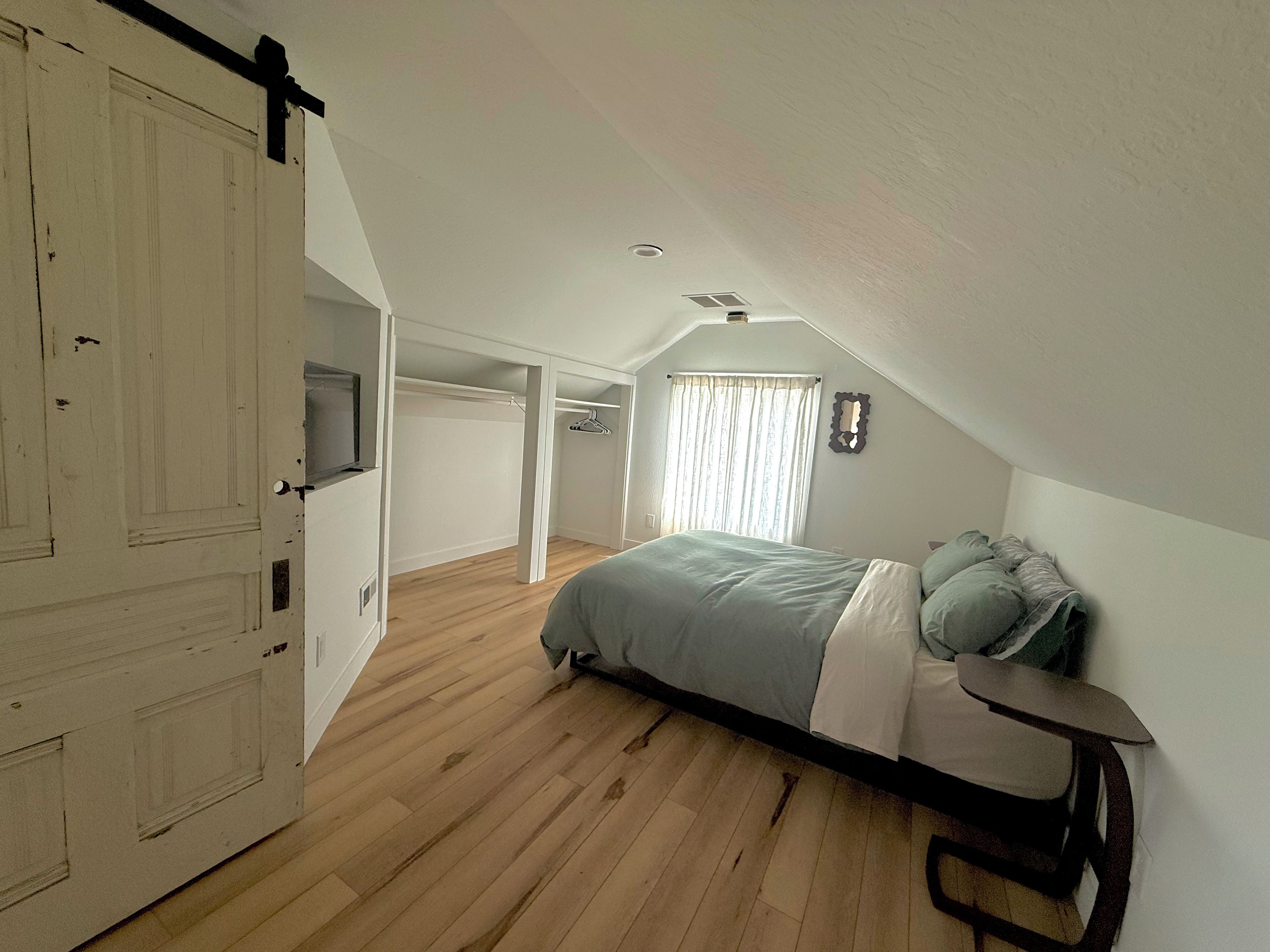 A bedroom with a bed, a wardrobe, a hanging coat rack, and a window with curtains.