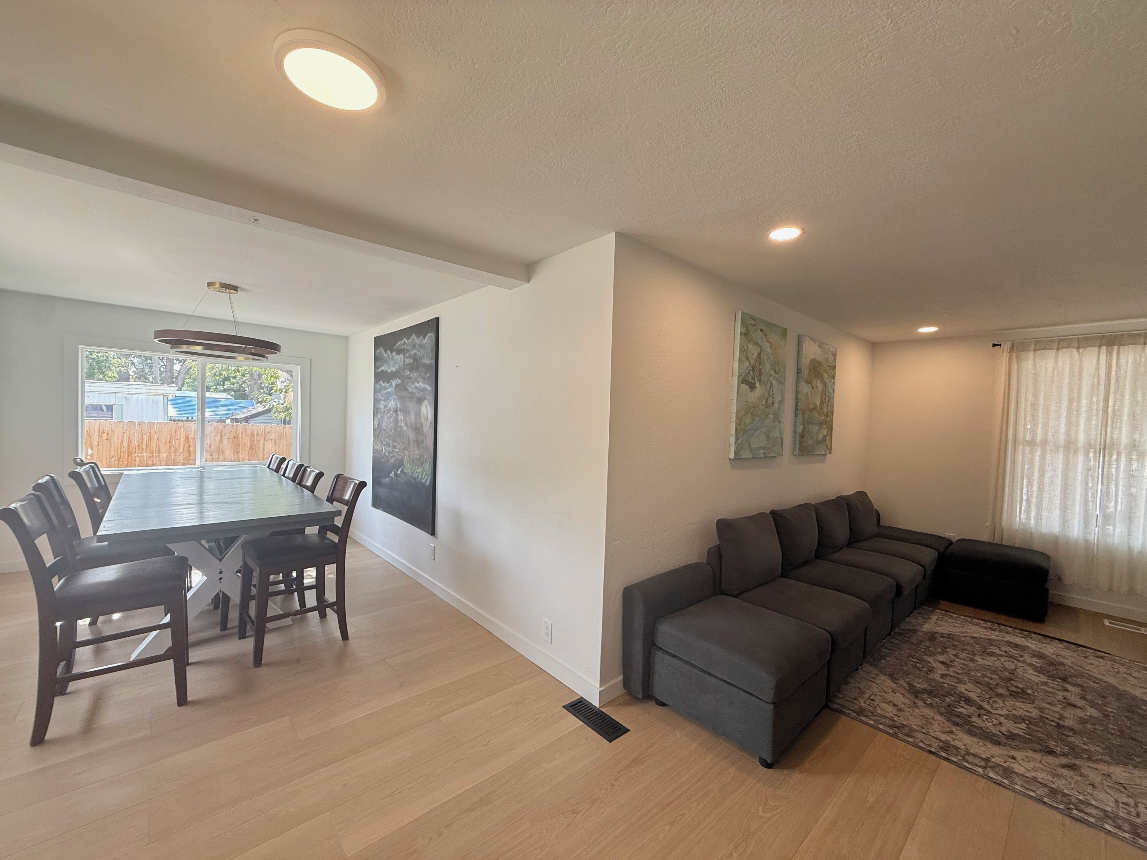 A modern living room with a dining area, a gray sectional sofa, and artwork on the walls.