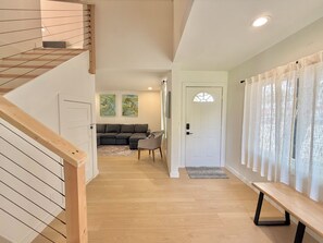 Um interior moderno com escadas, uma sala de estar com sofá e uma porta que dá para outro cômodo.
