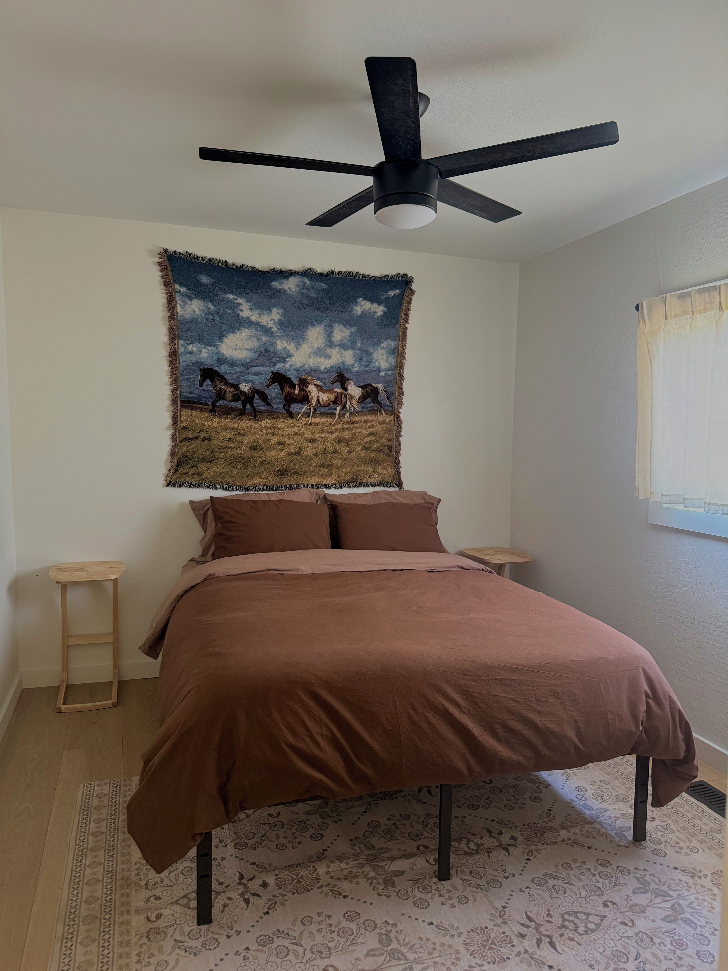 A bedroom with a bed, a ceiling fan, a tapestry, and a window.