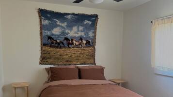 A bedroom with a bed, a ceiling fan, a tapestry, and a window.
