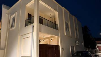 A two-story building with a balcony, a garage door, and a car parked in front.