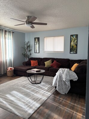 A living room with a dark brown sofa, a round coffee table, a ceiling fan, a window with blinds, and two framed pictures on the wall. - Find comfort and relaxation when experiencing your vacation (Twin Falls)