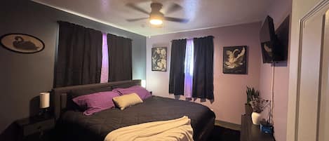 A bedroom with a bed, a ceiling fan, a nightstand, a TV, and a wall with artwork.