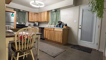Una cocina con armarios de madera, una mesa de comedor con sillas, un refrigerador y un microondas.