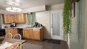 Une cuisine compacte avec des meubles en bois, une table à manger avec des chaises, une plante suspendue et une porte avec un store.