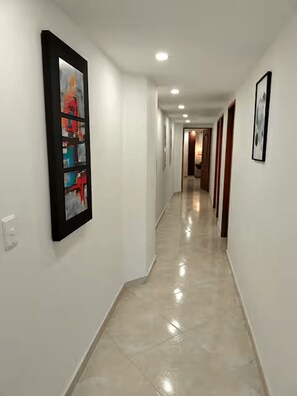 A long, narrow hallway with white walls and a shiny tiled floor. There are framed pictures on the walls and a door at the end of the hallway. - Exclusive, luxurious, centrally located apartment — serene and comfortable 302 (Medellín)