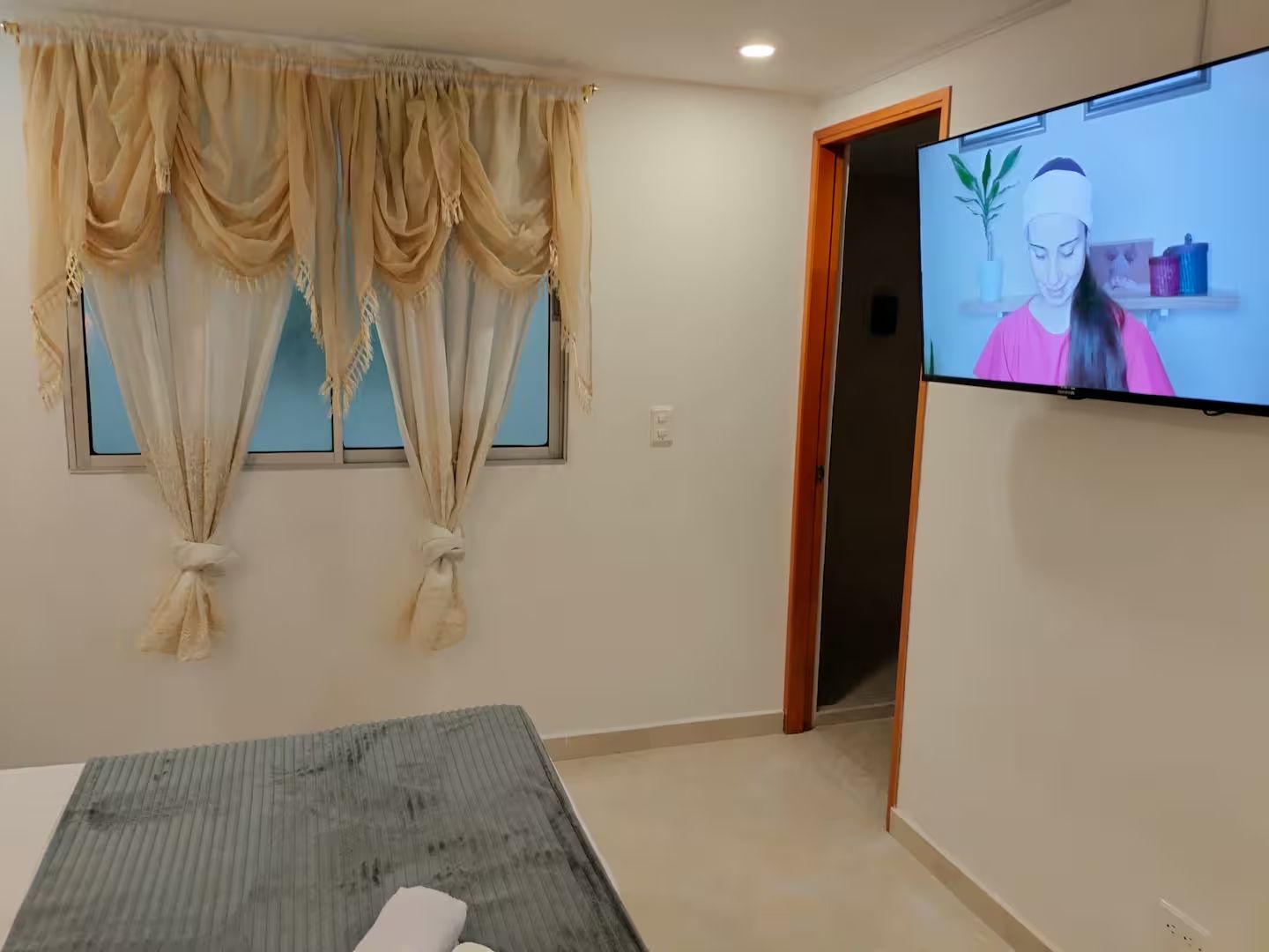 A hotel room with a bed, a television, and a window with curtains.