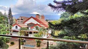 Un balcón con vistas a un edificio de techo rojo, rodeado de vegetación y un paisaje montañoso.
