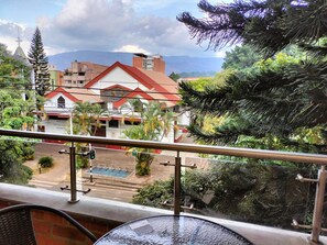 A balcony with a view of a building with a red roof, surrounded by greenery and a mountainous backdrop. - Exclusive, luxurious, centrally located apartment — serene and comfortable 302 (Medellín)