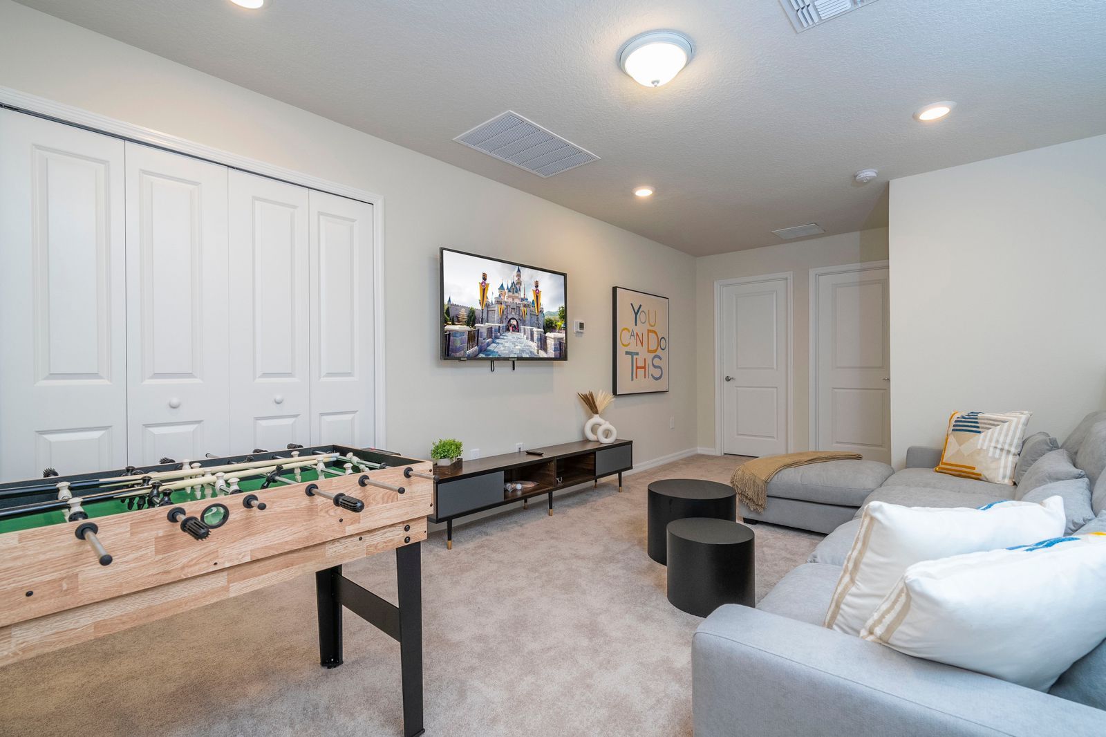 A living room with a foosball table, a gray sofa, a TV, and a motivational poster on the wall.