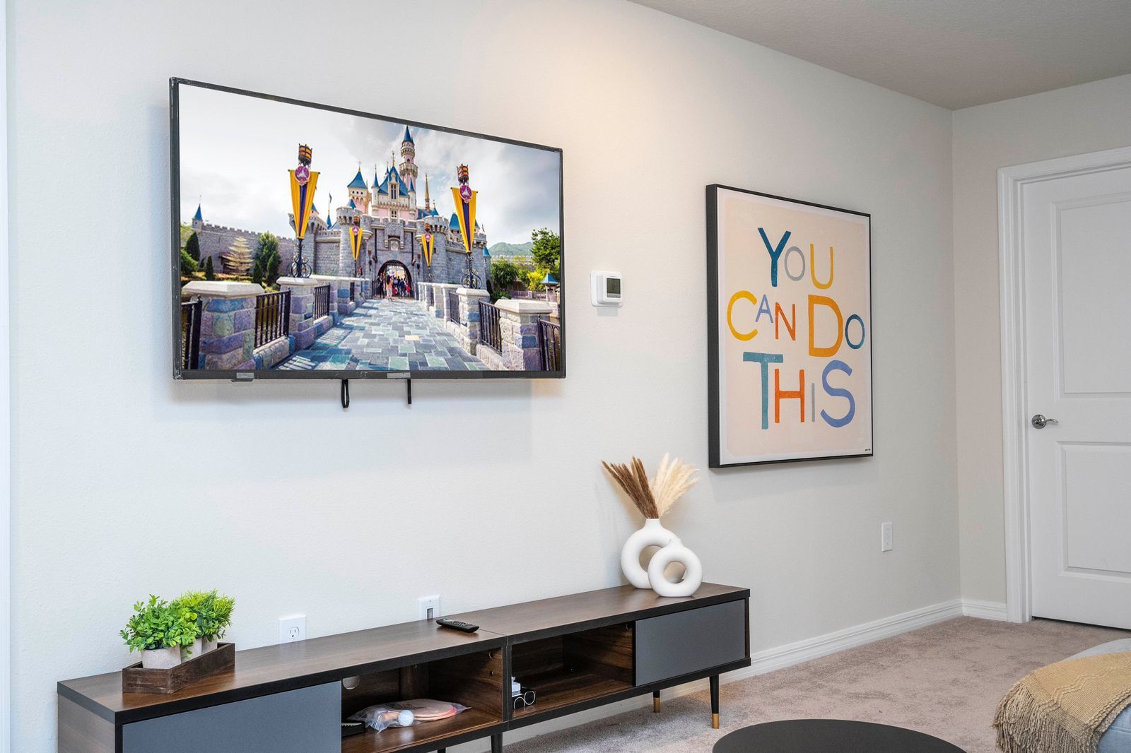 Une pièce dotée d’un téléviseur à écran plat fixé au mur, d’une console ornée d’objets décoratifs et d’une affiche inspirante.