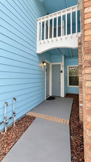 A house with a blue exterior, a front porch with a white railing, and a brick wall on the right. - 3BR Steps from Clubhouse Near Disney (Kissimmee)