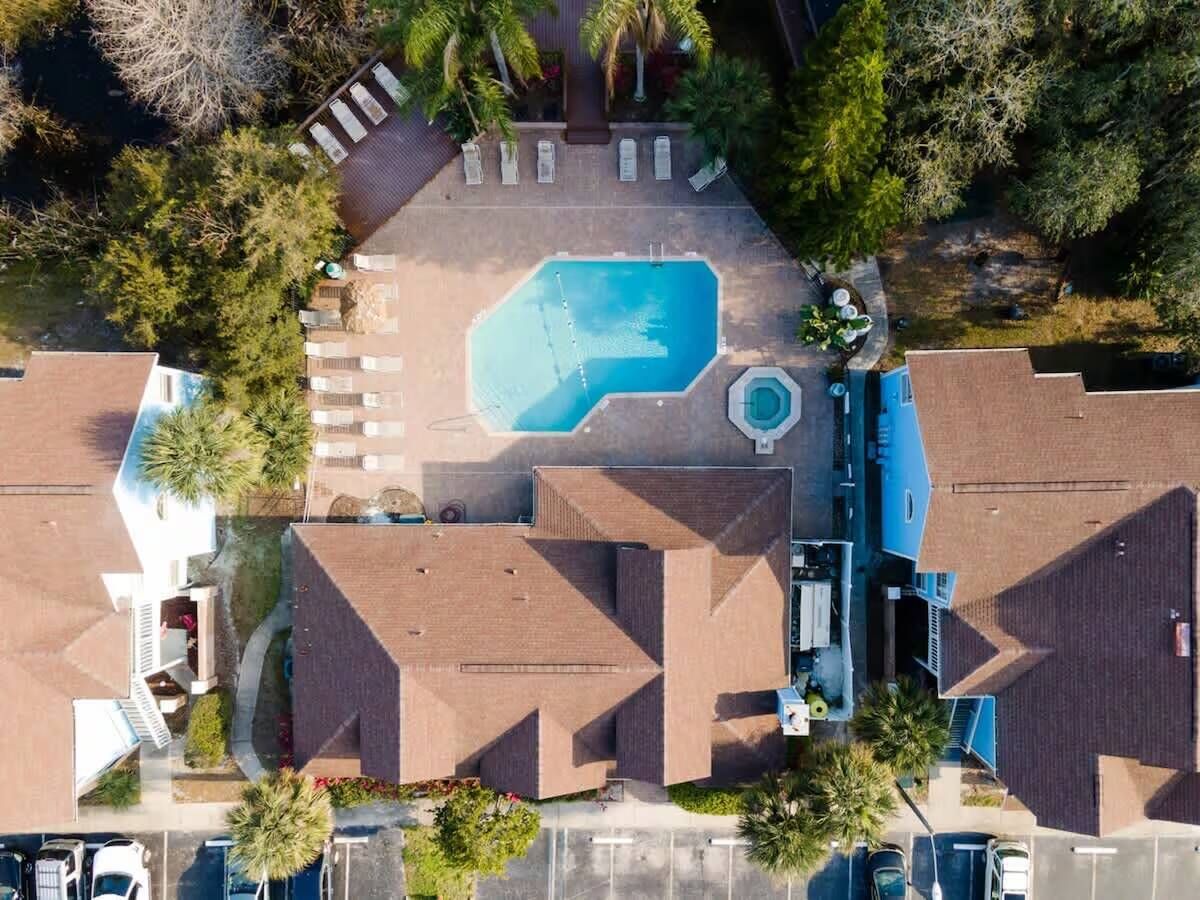An aerial view of a residential area with a swimming pool, multiple houses, and a parking lot.