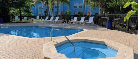 A swimming pool with a hot tub, lounge chairs, and a building in the background.