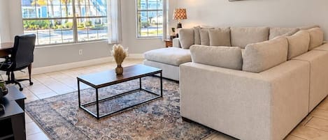 A living room with a sofa, coffee table, and a view of the outdoors through large windows.