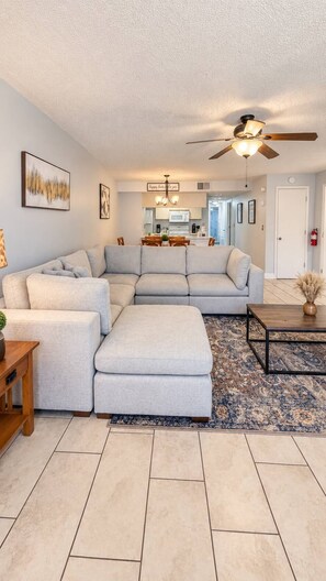 A living room with a sectional sofa, a coffee table, a rug, and a ceiling fan. - 3BR Steps from Clubhouse Near Disney (Kissimmee)