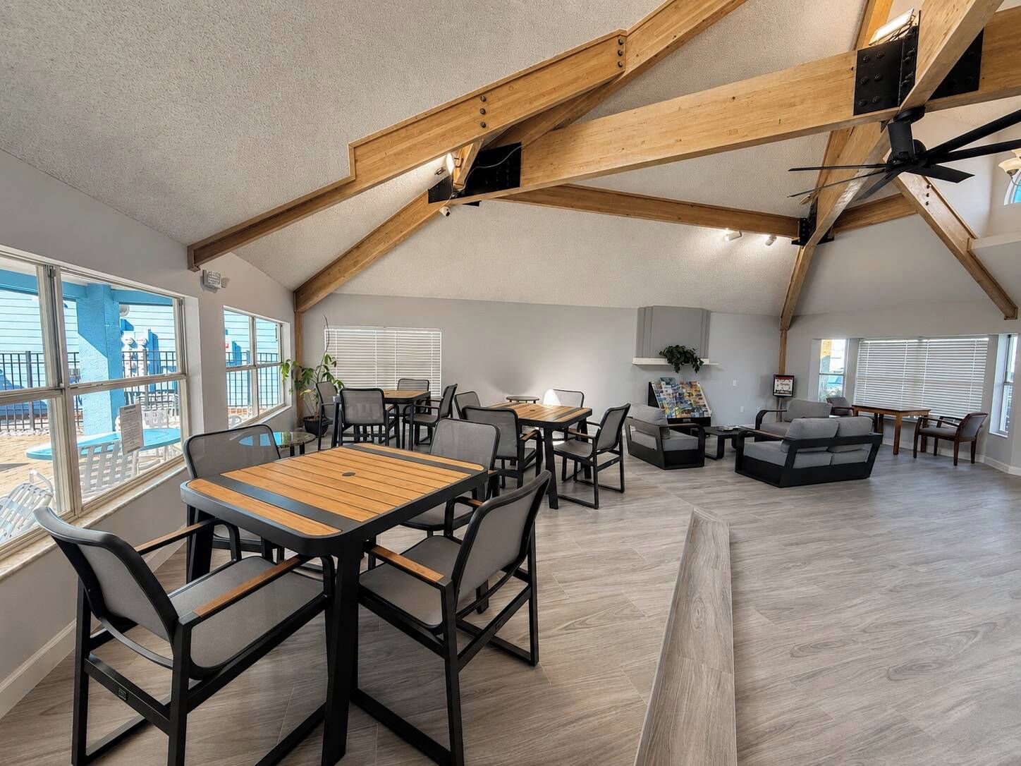 A spacious loft-style room with a high ceiling, exposed wooden beams, and a large window overlooking a deck.