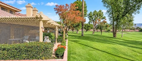 A well-maintained lawn, a patio area with outdoor furniture, and a variety of trees.