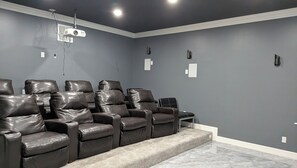 A home theater room with a dark gray wall, a ceiling-mounted projector, and leather reclining chairs.
