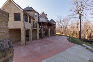 A large stone building with multiple levels, a covered front porch, and a driveway leading to a gated entrance. - Hillside Hideaway (Bentonville)