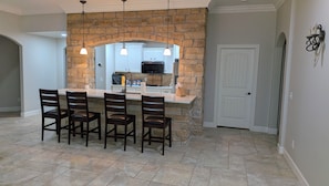 A dining area with a stone wall, a kitchen in the background, and a white door.
