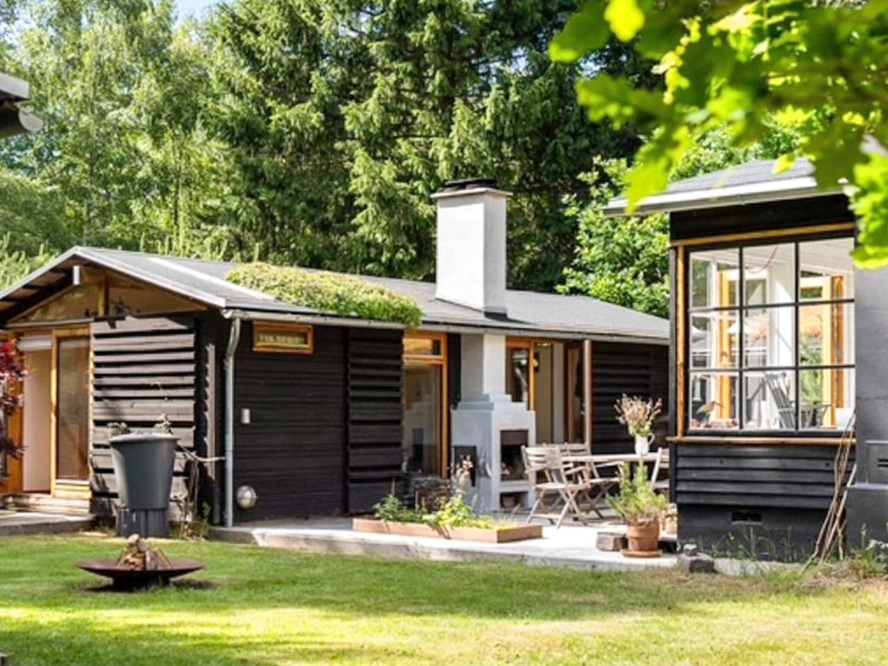 Uma cabana com chaminé, área de jantar com mobiliário de exterior e um pequeno jardim.