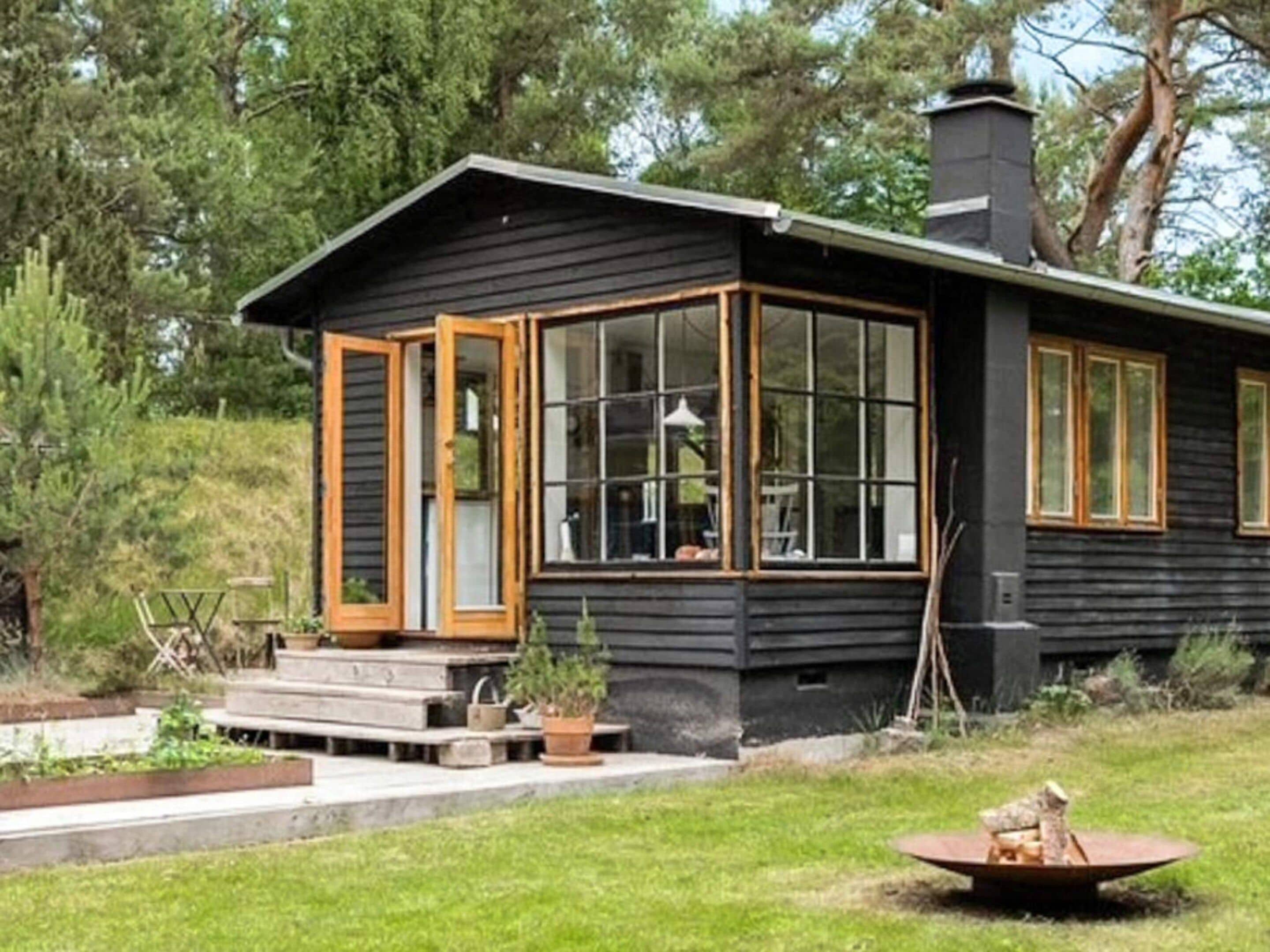 En stuga med ett stort fönster, en skorsten och en eldstad på gården.