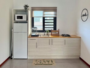 A compact kitchen with a microwave, refrigerator, and a window with blinds.