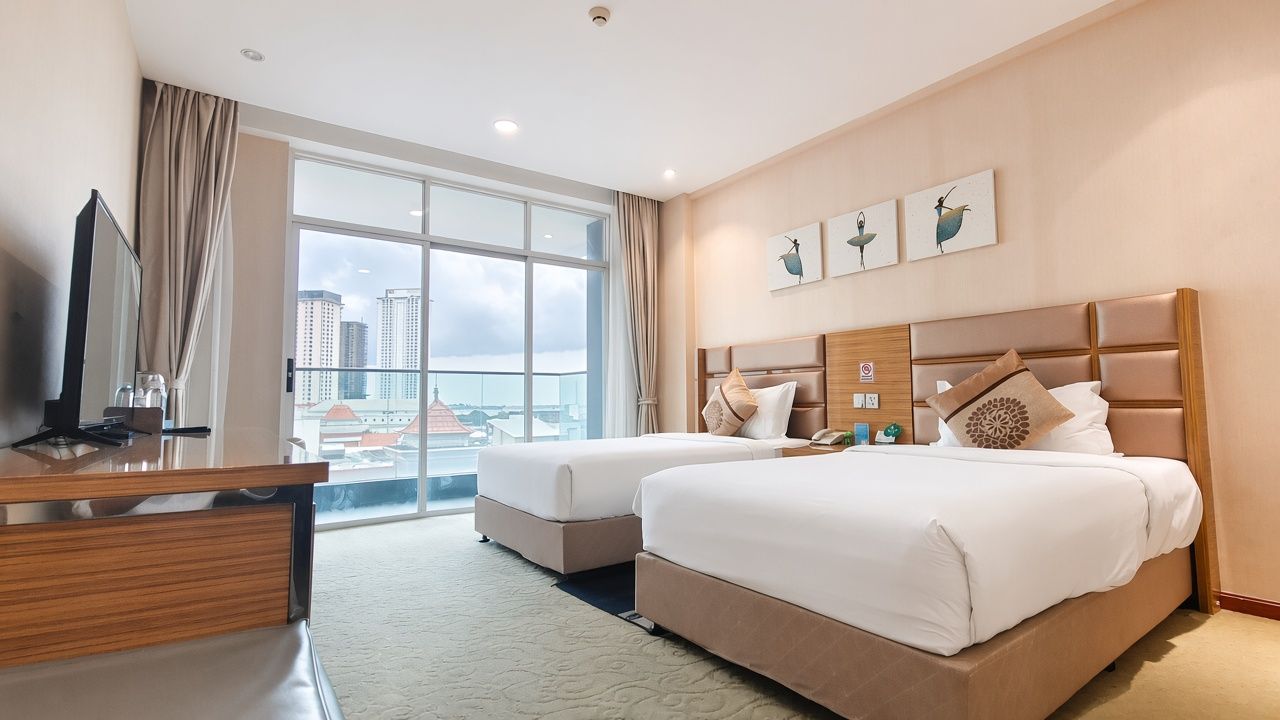 Habitación de hotel con dos camas, televisión y un amplio ventanal con vistas a la ciudad.